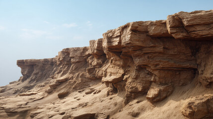 Fototapeta premium Eroded sandstone cliffs form a rugged, layered landscape against a clear, pale blue sky, showcasing the natural beauty and geological formations of arid terrain.