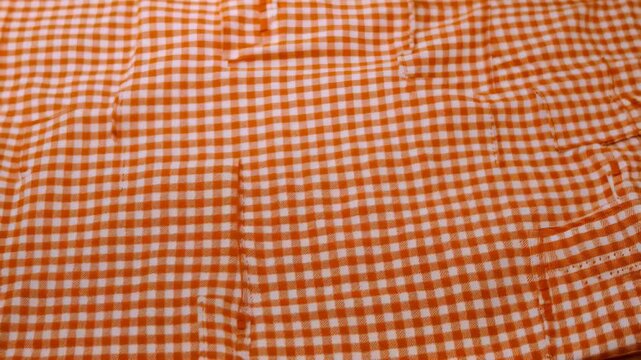Textile background featuring an orange and white gingham pattern with pocket detail and subtle texture