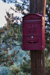 A classic red letterbox mounted on a pole in a rural or suburban setting. A symbol of traditional mail service, standing out vividly against its surroundings with nostalgic charm.