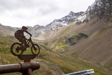 Rusty sculpture of a cyclist with the snow-capped mountains of Timmelsjoch in the background