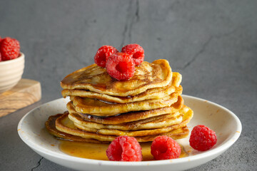 a close-up of a stack of golden banana pancakes on a white plate, topped with fresh raspberries and drizzled with syrup