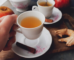 female hand holding white cup with apple tea on dark background on cold day