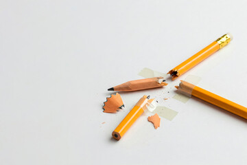Broken pencils glued together with tape on a light background. Space for text.