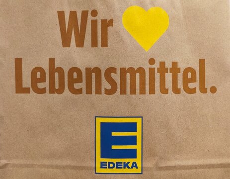 Closeup of a recyclable paper bag featuring the EDEKA logo, German branding, and a heart symbol representing the slogan "Wir lieben Lebensmittel" ("We love food").