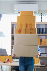 Fototapeta premium A young businesswoman who started her small SME business is lifting a large number of parcel boxes to be delivered to a shipping company to deliver the products to customers who have ordered them.