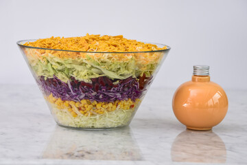 Fresh Seven Layer Salad in a clear glass bowl with layers of shredded lettuce, corn, red cabbage, green cabbage, creamy sauce bottle, and a crunchy crushed chips closeup side view of classic salad