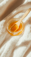 Golden sugaring paste in glass jar with wooden spatula on soft white towels, natural light, spa beauty concept, clean white background
