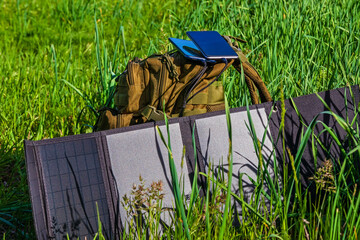 Portable solar panel folding on green grass near backpack. Solar power charging station for smartphones and personal devices