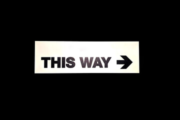 A clear directional sign THIS WAY on black background indicating the way forward