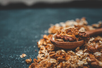 Close-up of wooden spoon with granola and walnut pieces on a dark textured background. Healthy snack made of oats and nuts in warm earthy tones