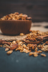 Granola and nuts in a small wooden spoon with a blurred bowl in the background. Rustic style breakfast concept with healthy ingredients on dark surface