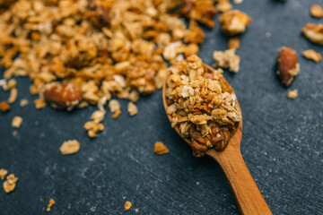 Close-up of wooden spoon with granola and walnut pieces on a dark textured background. Healthy snack made of oats and nuts in warm earthy tones