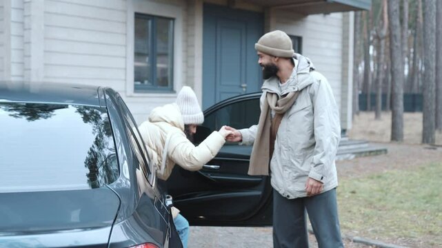 A Black man in his 20s, letting his mid-20s Latina girlfriend out of the car and helping her politely, as they're parked next to a house, and then getting to the trunk to unload their groceries