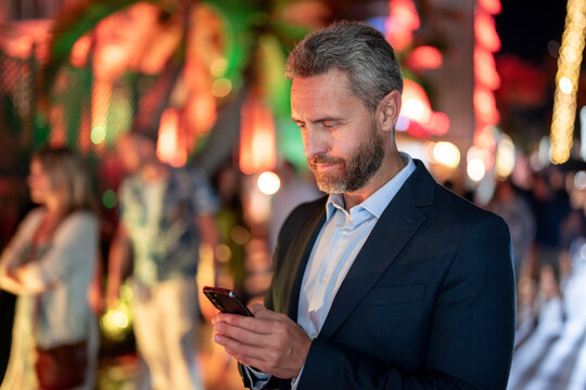 Businessman talk on phone at night city. Businessman in suit with phone in city. Business man using phone. Businessman call phone near city lights. Business call. Rich businessman in luxury setting.