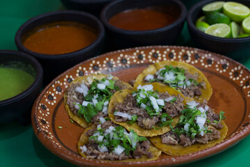 A vibrant plate of delicious tacos filled with seasoned beef, topped with fresh cilantro and onions, served with a variety of flavorful salsas and lime wedges on the side.