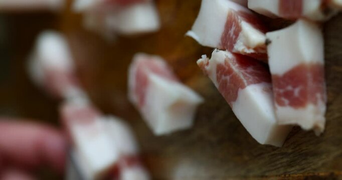 Close-up of a man's hand slicing guanciale, showcasing the rich texture and marbling of the cured meat
