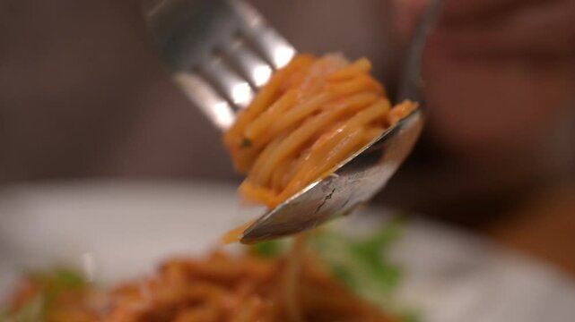 Twirling metal fork gathering spaghetti with vibrant tomato sauce, lifting pasta from white ceramic plate in elegant dining setting