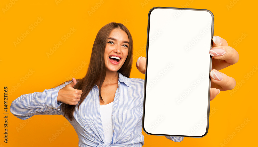 Poster Recommendation. Portrait of excited lady holding big smartphone with white blank screen in hand, showing close up to camera making thumb up gesture. Gadget with empty free space for mock up, banner