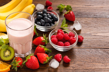 Top view of glass with pink fruit smoothie surrounded by fresh berries bananas kiwi orange and mint leaves on rustic wooden tablewith copy space