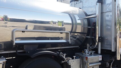 Close up of a shiny semi truck side fuel tank with a mounted step platform reflecting light to showcase industrial transportation details