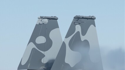 Close up of twin tail rudders on a fighter jet painted in camo piercing through a clear sky Aerospace power at its finest