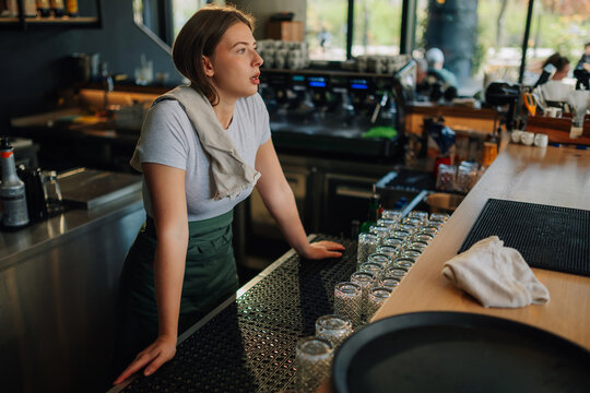 Bored barista leaning on counter waiting for customers in empty bar