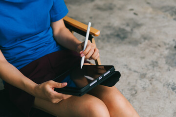 Person Using Digital Tablet with Stylus in Relaxed Indoor Setting on a Comfortable Chair