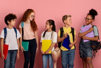 Cute schoolkids of different races and ages looking at each other over pick background