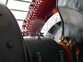 Close-up of a vintage electric generator showing heavy black metal housing, red copper coils, and brass connectors, captured inside an industrial setting with daylight