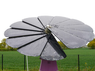 Large flower-shaped solar panel installation with petal-like photovoltaic segments stands in a green field near a fence, designed to track the sun for optimal energy capture