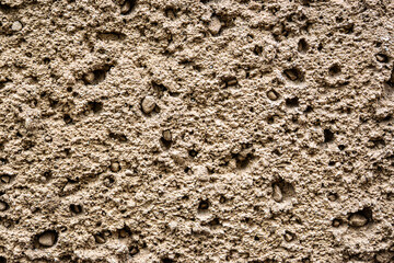 Detailed close-up of a rough, porous wall texture with uneven surface and embedded pebbles. Ideal for backgrounds, design, or 3D texture mapping.