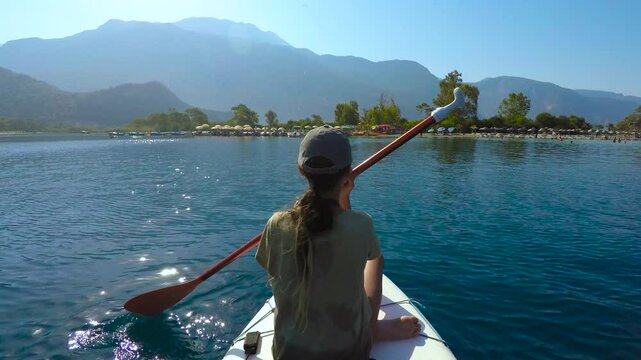 Tourist paddling on a sup board in the calm sea near the beach. Young woman paddling on stand up paddle board across calm turquoise sea, near scenic mediterranean coastline