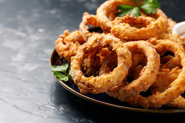 Homemade deep fried onion rings on plate with sauce.