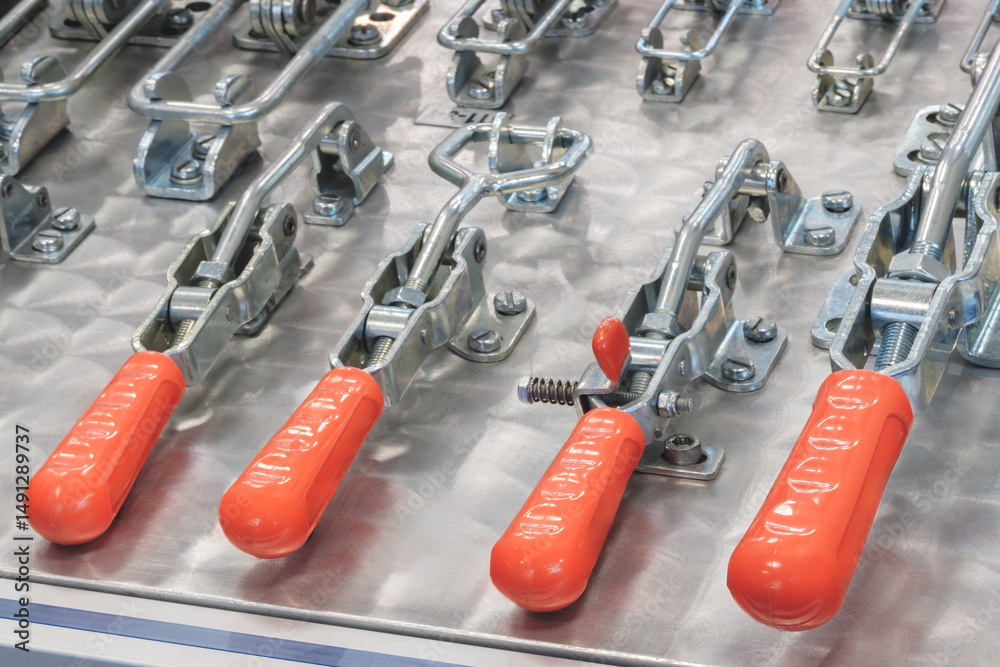 Poster a row of red and silver metal clamps are lined up on a table. the clamps are all different sizes and