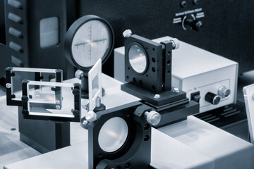 Optical equipment including telescope and lenses are displayed on a table in a laboratory. Optics and photonics concept science experiment with laser background