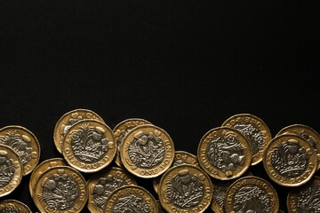 Scattered British one pound coins lined along the bottom of a black background, symbolising savings, wealth, and UK currency, Stafford, United Kingdom, May 18, 2025..