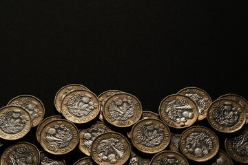 Scattered British one pound coins along the lower edge of a black background, representing savings, earnings, and UK currency, Stafford, United Kingdom, May 18, 2025..