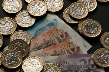 British banknotes and one pound coins scattered on a dark surface, representing UK currency, cash flow, and financial wealth, Stafford, United Kingdom, May 18, 2025..