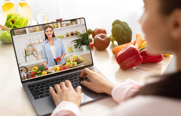 Young woman using laptop computer to take part in online culinary workshop, learning vegan cuisine recipes on web from home. Millennial lady watching cooking tutorial on internet