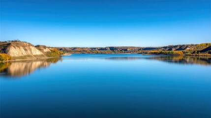 Serene lake reflecting autumnal hills under a vast blue sky.