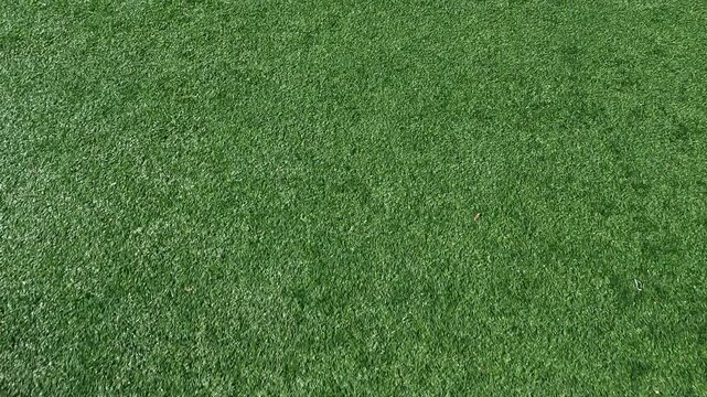 Slow motion views moving across a green artificial turf football or soccer field with yard line markings. Focus on the end zone. Overhead view.