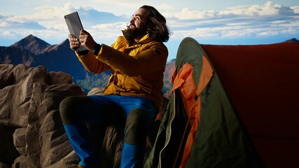 Reckless explorer struggling with wind and weak signal keep internet connection, camping on a scenic rocky mountain peak. Hiker in danger with extreme cold weather, foolish. Camera A.