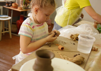 Kids arts and crafts class in workshop. Little girl creating cup and bowl of clay. Creative activity for young children in school. Cute kid forming toy with ceramic.