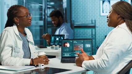 Fototapeta premium Young girl with a pulmonary infection asking medic for professional advice, discussing about medicine to help with coughing or breathing. African american patient and doctor at clinic. Camera A.