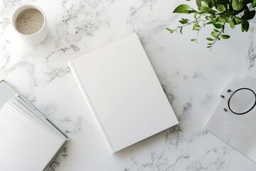 Overhead view of a blank white book on a marble surface, accompanied by a coffee cup, plant, and papers