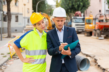 Civil engineer and a young woman worker working on a construction site discuss a construction plan, make important notes ..on tablet