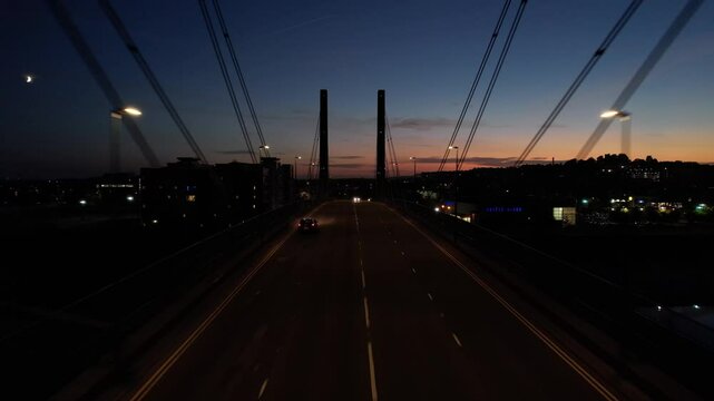 Traffic on cable stayed bridge over river, silhouette against twilight sky