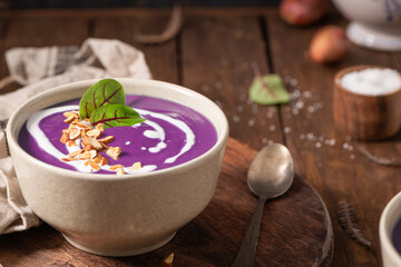 Healthy creamy red cabbage soup topped with herbs, a swirl of cream, toasted almonds, and fresh herbs, resting on a rustic wooden board.