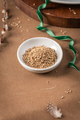 Fennel seeds in a white bowl on a textured brown surface with a delicate feather and blurred plant stem in the background