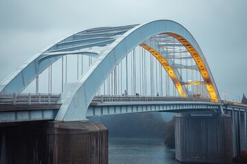 Fototapeta premium Large steel arch bridge over calm river under cloudy sky with subtle warm lighting on one side